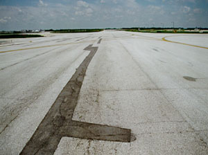 Overview of a long, narrow, wandering patch at the centerline of a taxiway pavement.             There is noticeable cracking within the patch area.