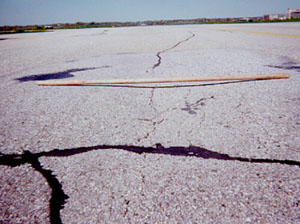 Overview photo of a pavement with a visible area of high-severity rutting.           A 6-ft (2-m) long piece of wood has been placed across the rut to show the depth of the rut.