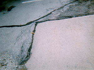 Overview photo showing an asphalt surface around the corner of a PCC slab.           The asphalt at the joint between the PCC and asphalt surfaces is noticeably higher than the PCC slab.