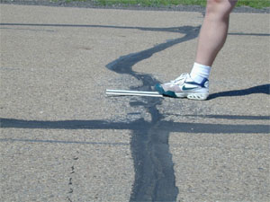 Close-up photo of a transverse joint with a slight but visible swell in the pavement surface at the joint.           A ruler has been placed across the joint in the longitudinal direction to show that there is an upward bulge in the pavement at the joint.