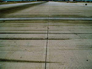 Overview photo showing a corner where four PCC slabs come together. Three of the four slabs in the photo have low-severity           corner breaks. Each corner break is a fairly tight, single, non-spalled crack.