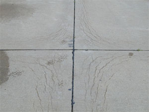 Close-up photo showing a corner where four PCC slabs come together. All four slab corners           in the photo show a series of crescent-shaped D-cracks. The cracks are all tight with no visible spalling.