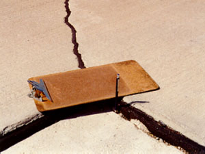 Close-up photo showing a transverse joint with a 1 1/2 in (38 mm) difference in elevation across the joint.           A clipboard is placed across the joint in the photo to illustrate that there is a height differential between the two slabs.