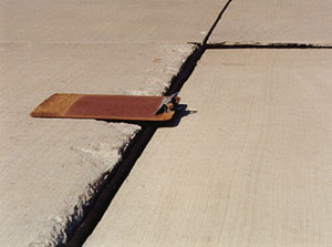 Close-up photo showing a transverse joint with a 1/2 in (13 mm) difference in elevation across the joint.           A clipboard is placed across the joint in the photo to illustrate that there is a height differential between the two slabs.