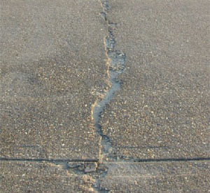 Close-up photo of a single high-severity crack in a PCC slab. The crack appears to be greater than 1 in (25 mm) wide           and shows areas of spalling with high FOD potential.