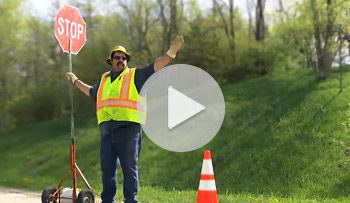 Flagger standing to the side behind cone.